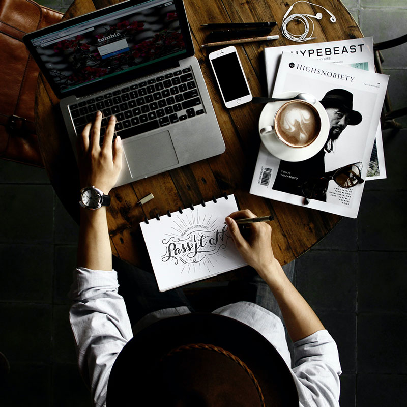 Overhead view of a virtual assistant graphic designer drawing and using laptop